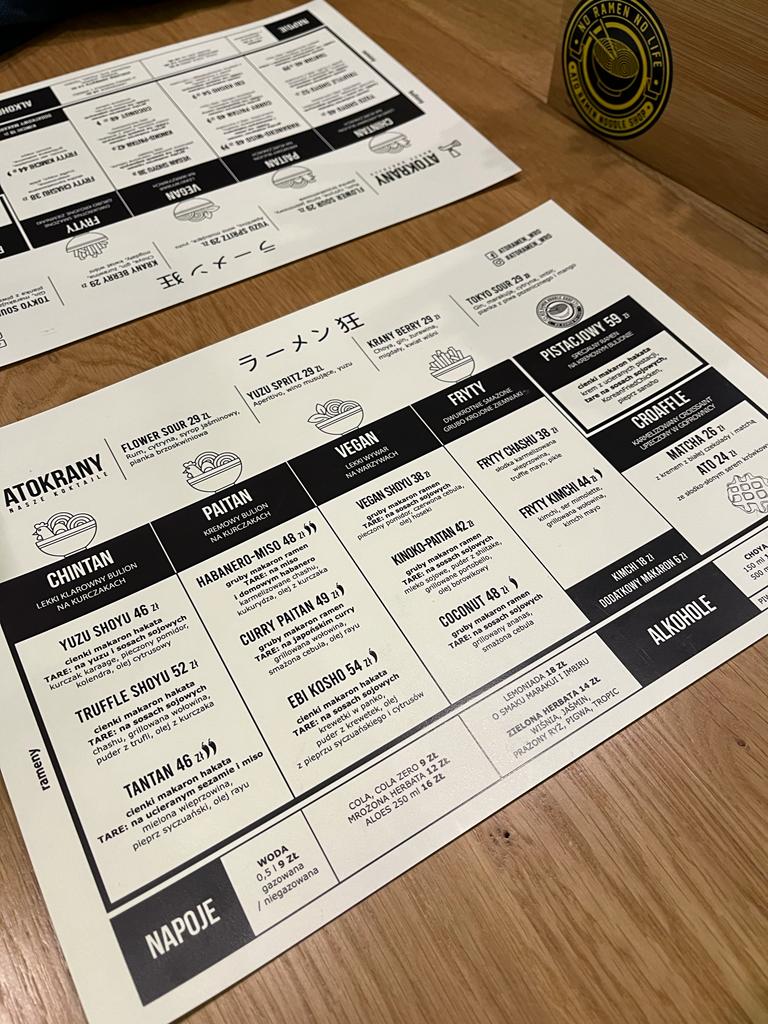Czarno białe menu Ato Ramen leżące na drewnianym blacie