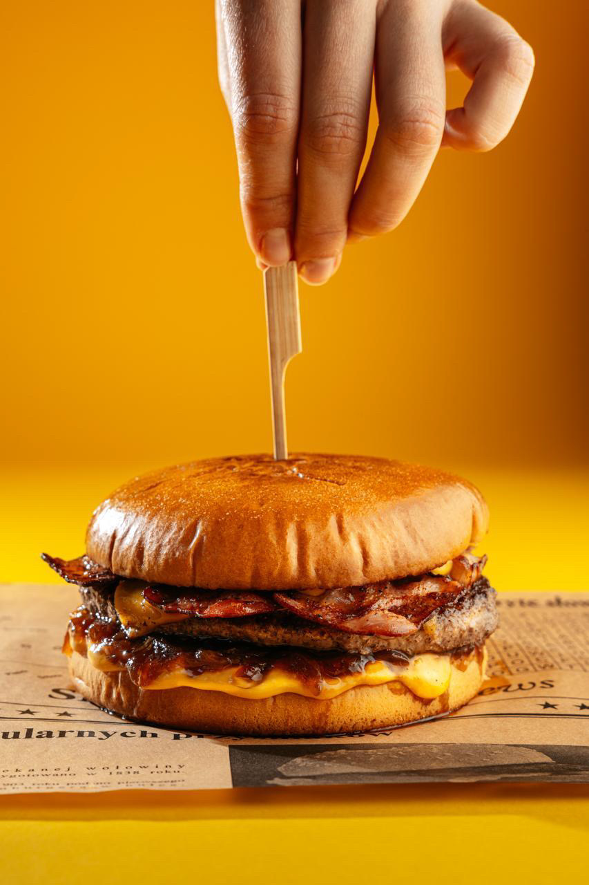 Burger Smakosza – bułka brioche, 100% wołowina, cheddar, trzy plastry grillowanego boczku, cebulowy konfit oraz sos cheddar — Pierre Dolle